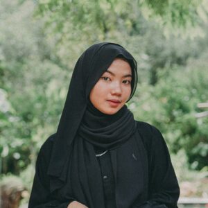 a woman wearing a black hijab standing in front of a tree