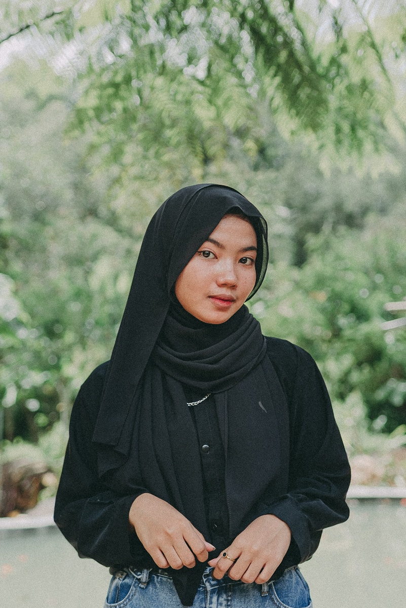 a woman wearing a black hijab standing in front of a tree